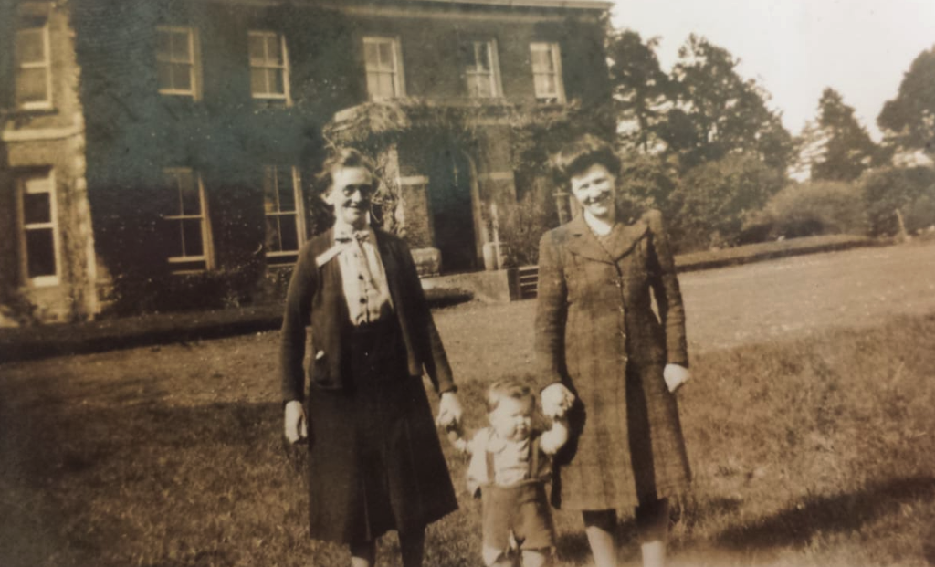 Two women and a child stand in front of Cloona House in a sepia photo from around the second world war